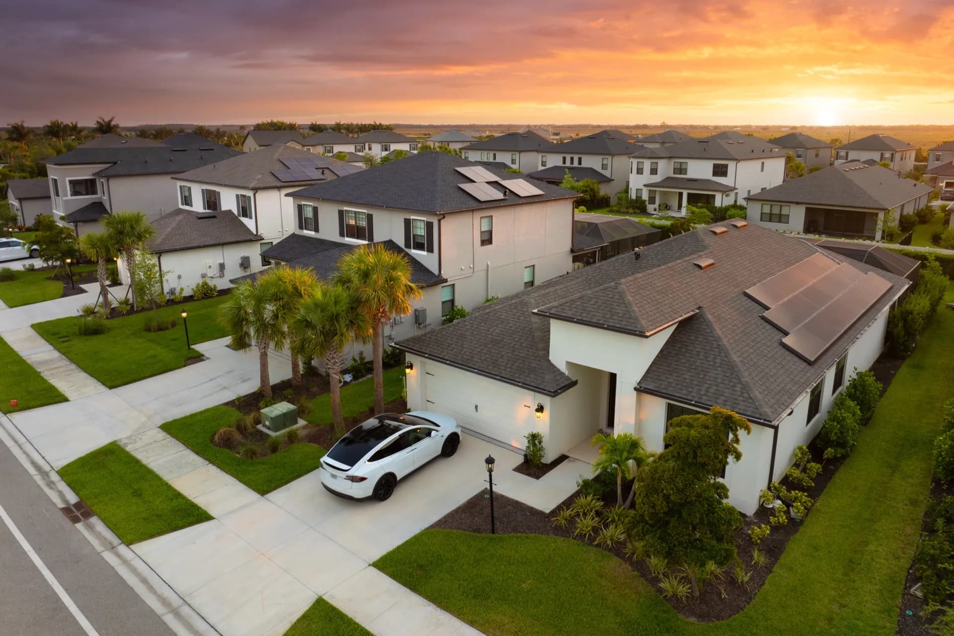 Aerial view of a neighborhood at sunset with solar panels on several rooftops