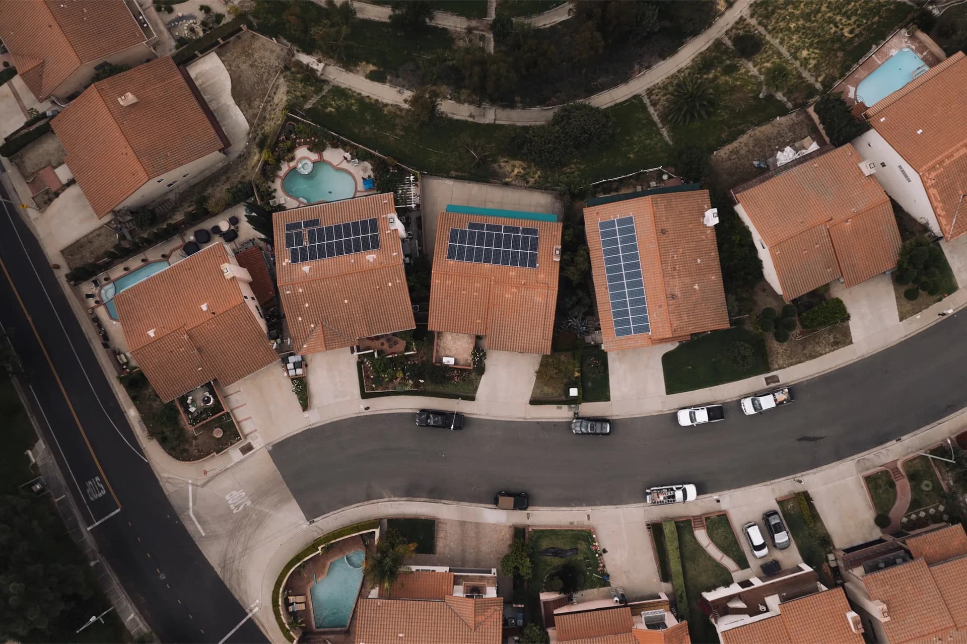 Overhead aerial view of a neighborhood street with solar panels on several tile rooftops