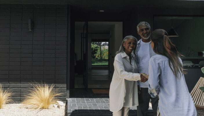 A warm welcome at the front door as a smiling couple greets a visitor.